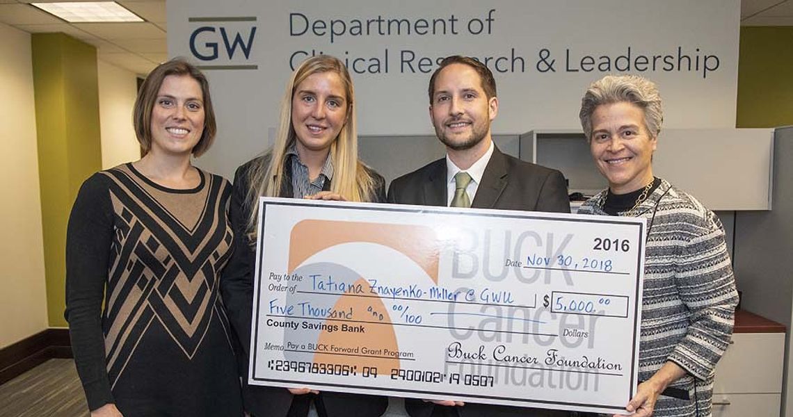 four people standing in the Department of Clinical Research & Leadership holding a large check