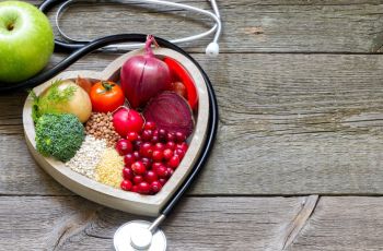 heart shaped box filled with vegetables and surrounded by a stethoscope and an apple