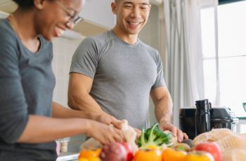 Two people cooking with vegetables in a kitchen and smiling